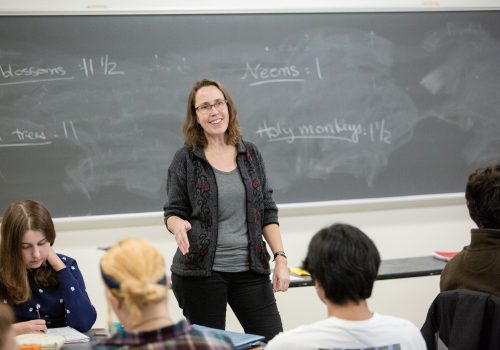 A professor lecturing students with a chalkboard in the background.