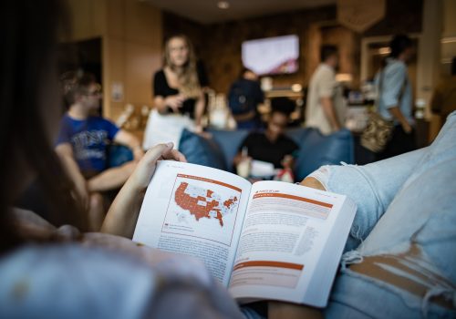 A student reading a textbook with a map of the U.S. with some states highlighted in red.